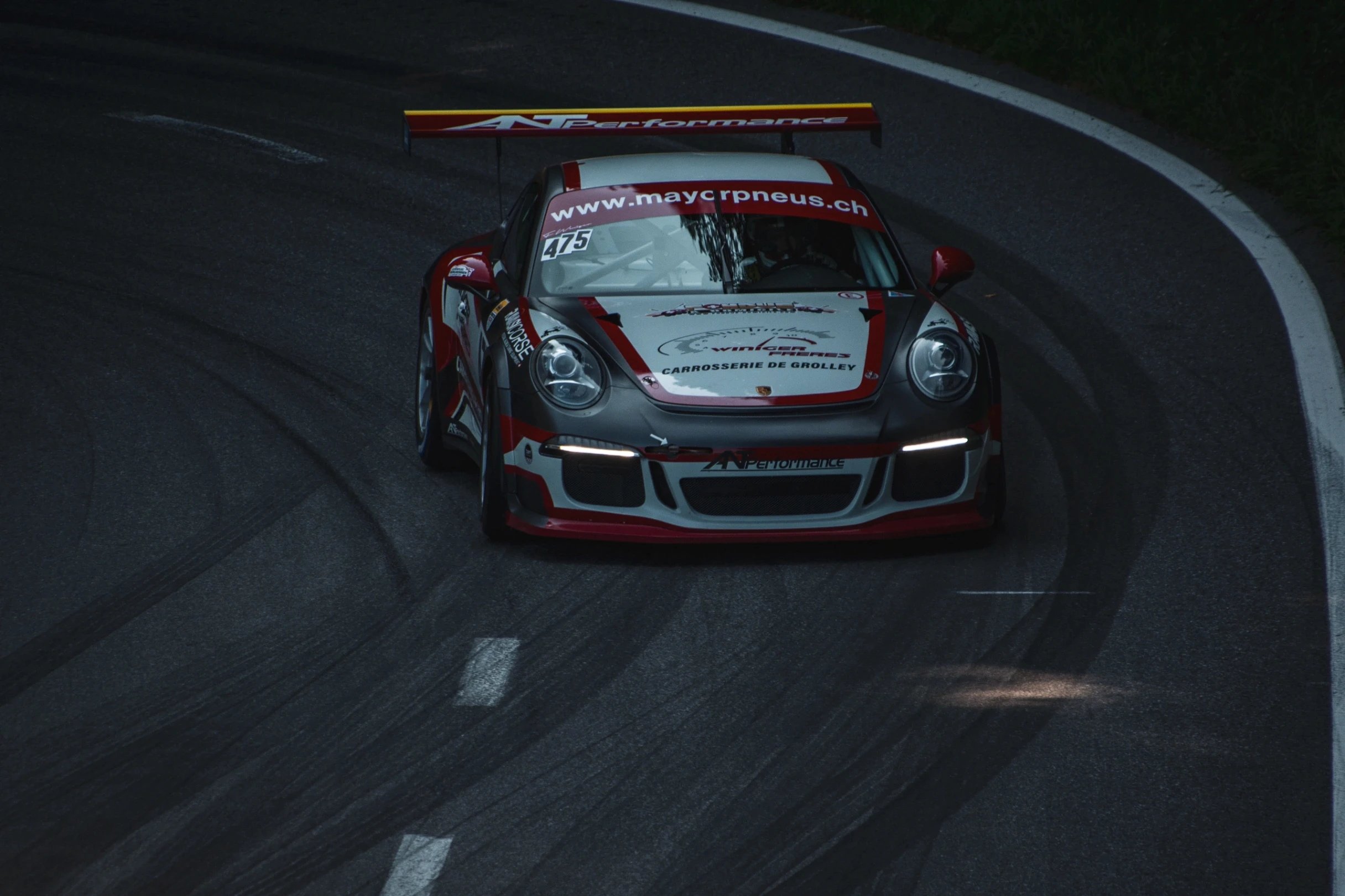 Porsche race car with sponsor logos on a dark asphalt track.