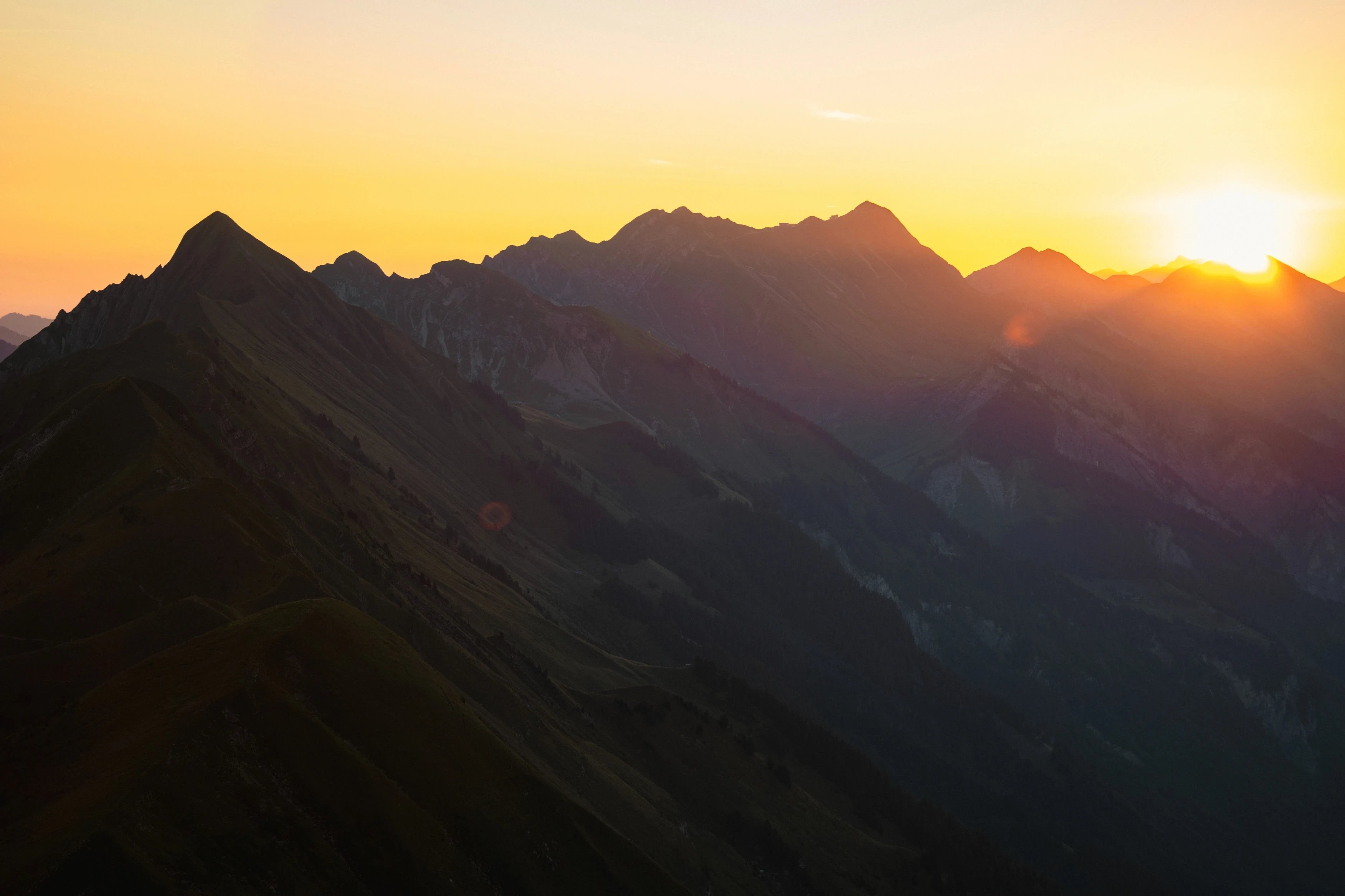 Sunset over jagged mountain peaks, casting long shadows.