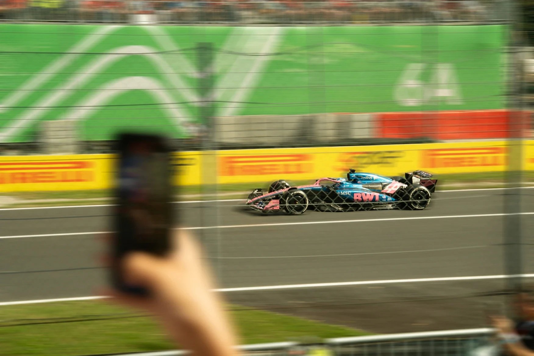 Alpine f1 car on a blurred track, filmed on a phone.